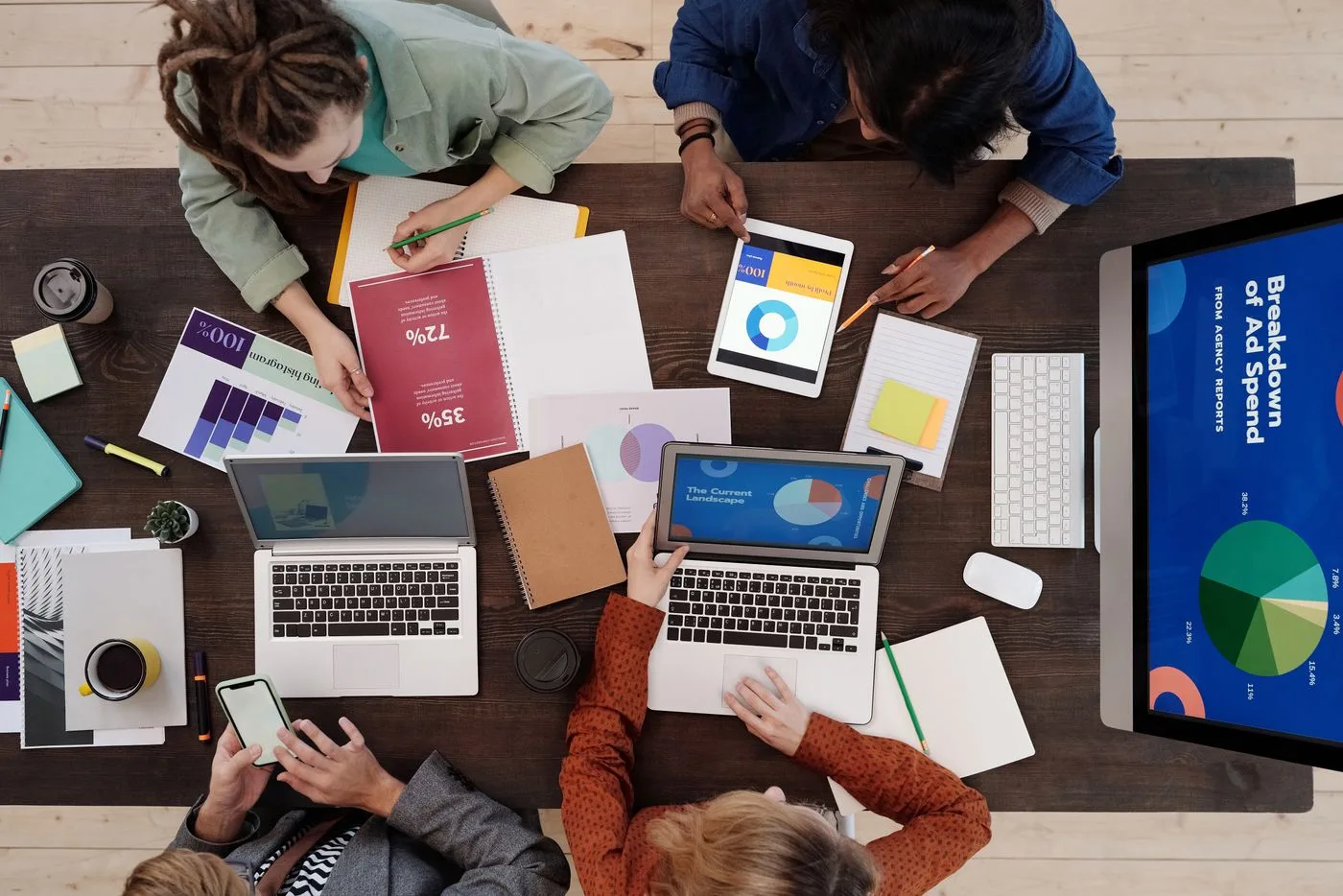 Equipo reunido alrededor de una mesa con computadoras, gráficos y notas de trabajo.