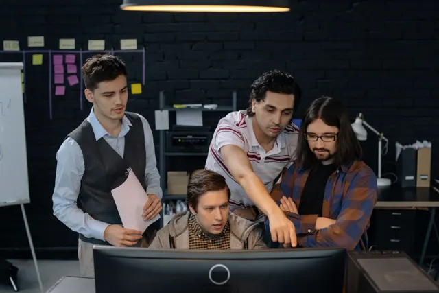 Cuatro personas revisan juntas una pantalla de computadora en una oficina.