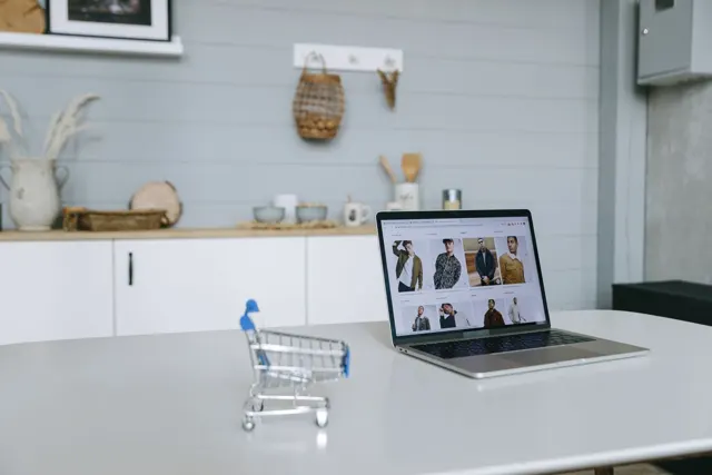 Laptop con una tienda de ropa en pantalla y un carrito de compras en miniatura.